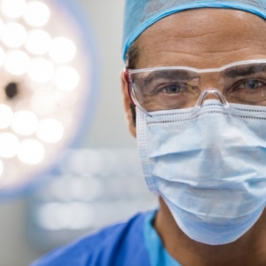 Surgeon with protective mask; Close up face of surgeon man looking at camera with protective mask. Dental assistant with surgical mask and safety glasses in dental clinic. Happy successful surgeon in a operating room.